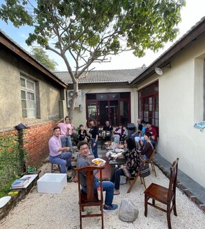 A group of people seated around a table in an outdoor patio area with a tiled roof, surrounded by a low brick wall and a tree. - A Touch of Zen ─ A Restored Japanese Colonial Era Guest House (Kaohsiung)