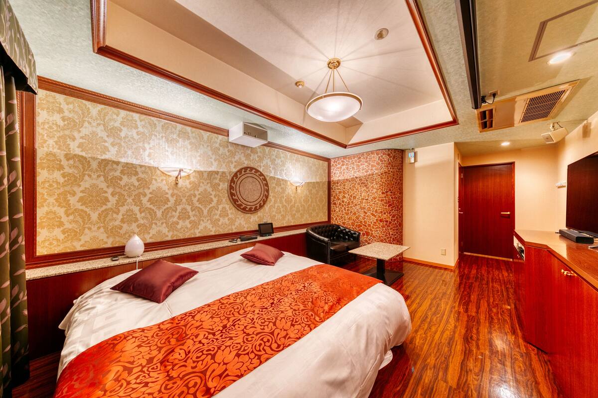 A hotel room with a large bed, a desk, a chair, a TV, and a wardrobe.