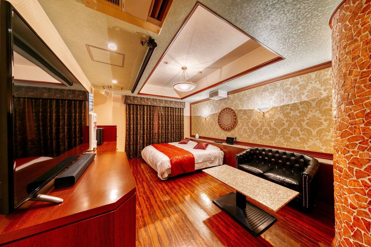 A hotel room with a bed, a sofa, a desk, and a mirror.
