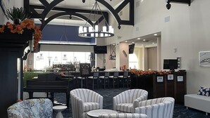En rummelig lobby med barområde, siddepladser og et flygelsk.