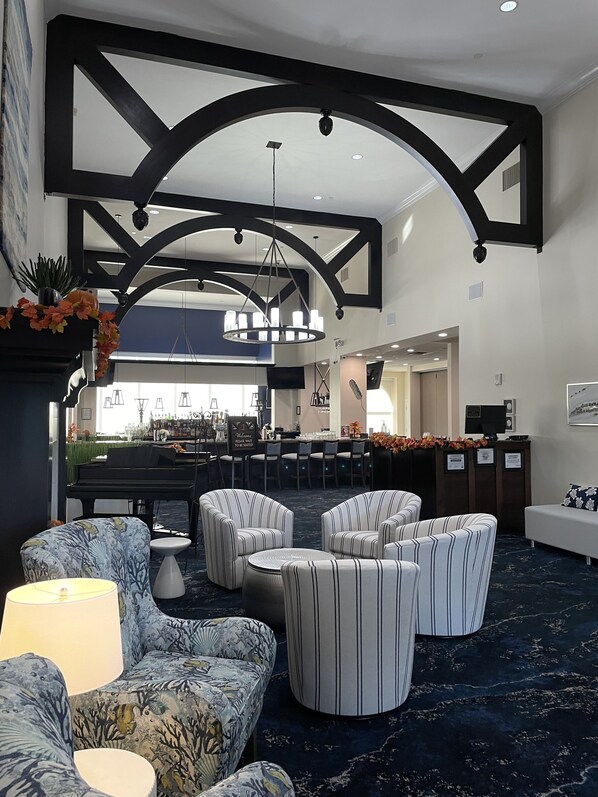 A spacious lobby with a bar area, seating arrangements, and a piano.