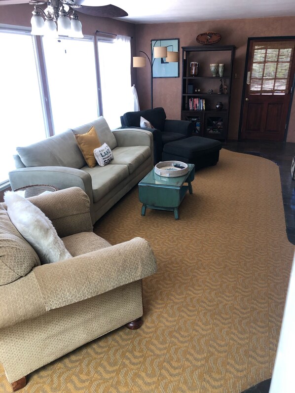 A living room with a sofa, armchair, and ottoman, a coffee table, and a bookshelf.