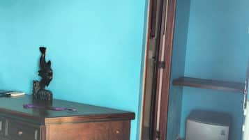 A room with a wooden desk, a chair, a small refrigerator, and a shelf with an air conditioner.
