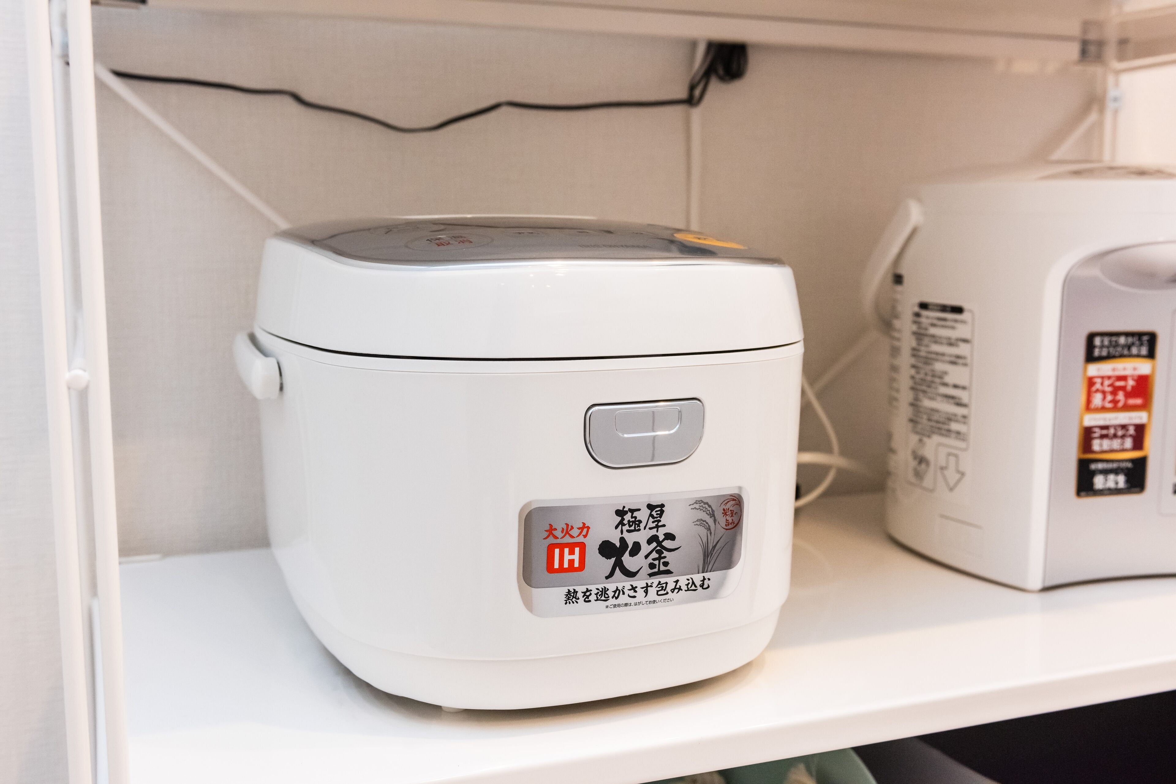 Una cocedora de arroz blanca con texto en japonés y un botón de encendido en la parte frontal.