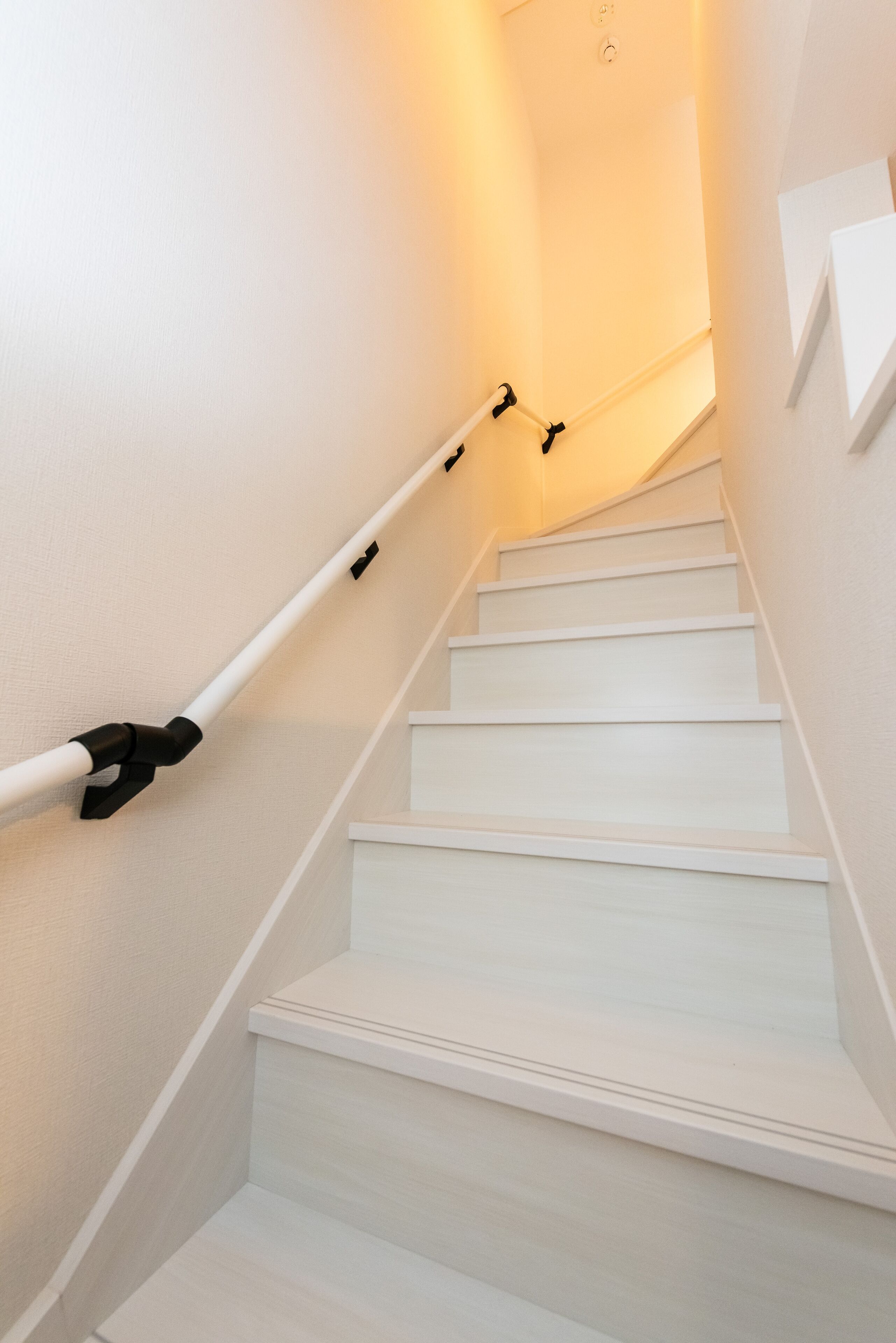 A staircase with white steps and handrails, leading to a landing with a light fixture.