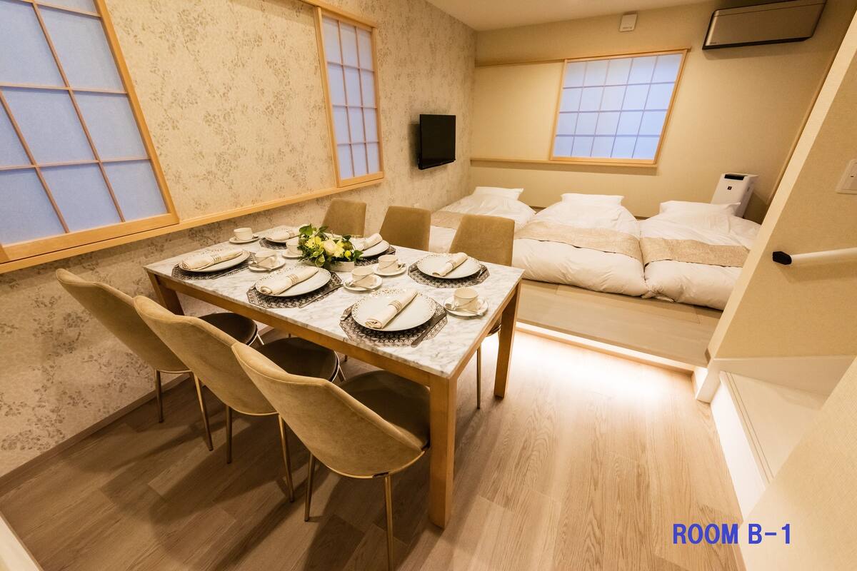 Un comedor con una mesa dispuesta para cuatro, un sofá al fondo y un televisor montado en la pared.