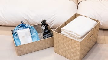 Two wicker baskets on a bed, one with a blue bag and a spray bottle, the other with folded white towels.