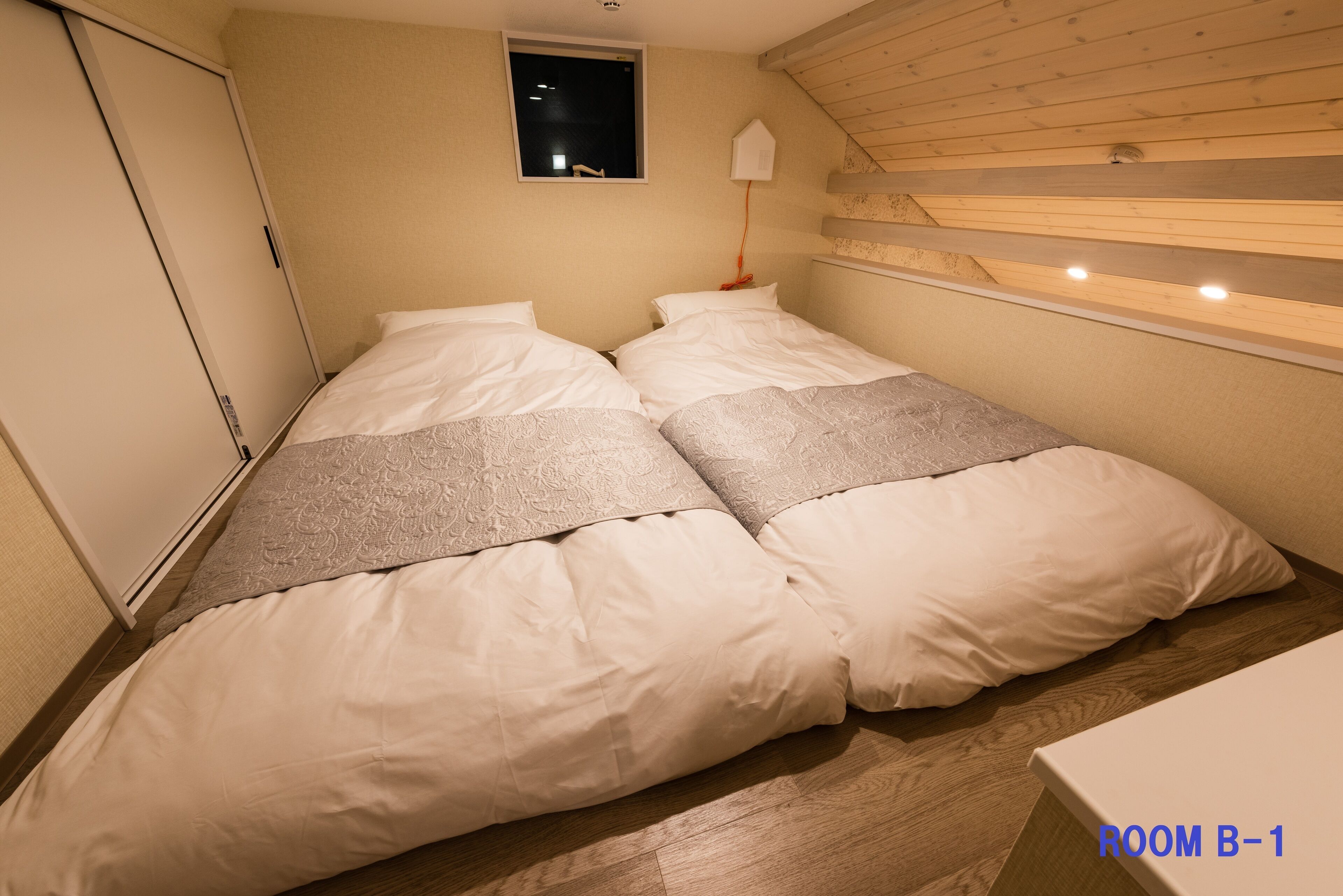 A bedroom with two beds, a window, a night light, and a wooden ceiling.