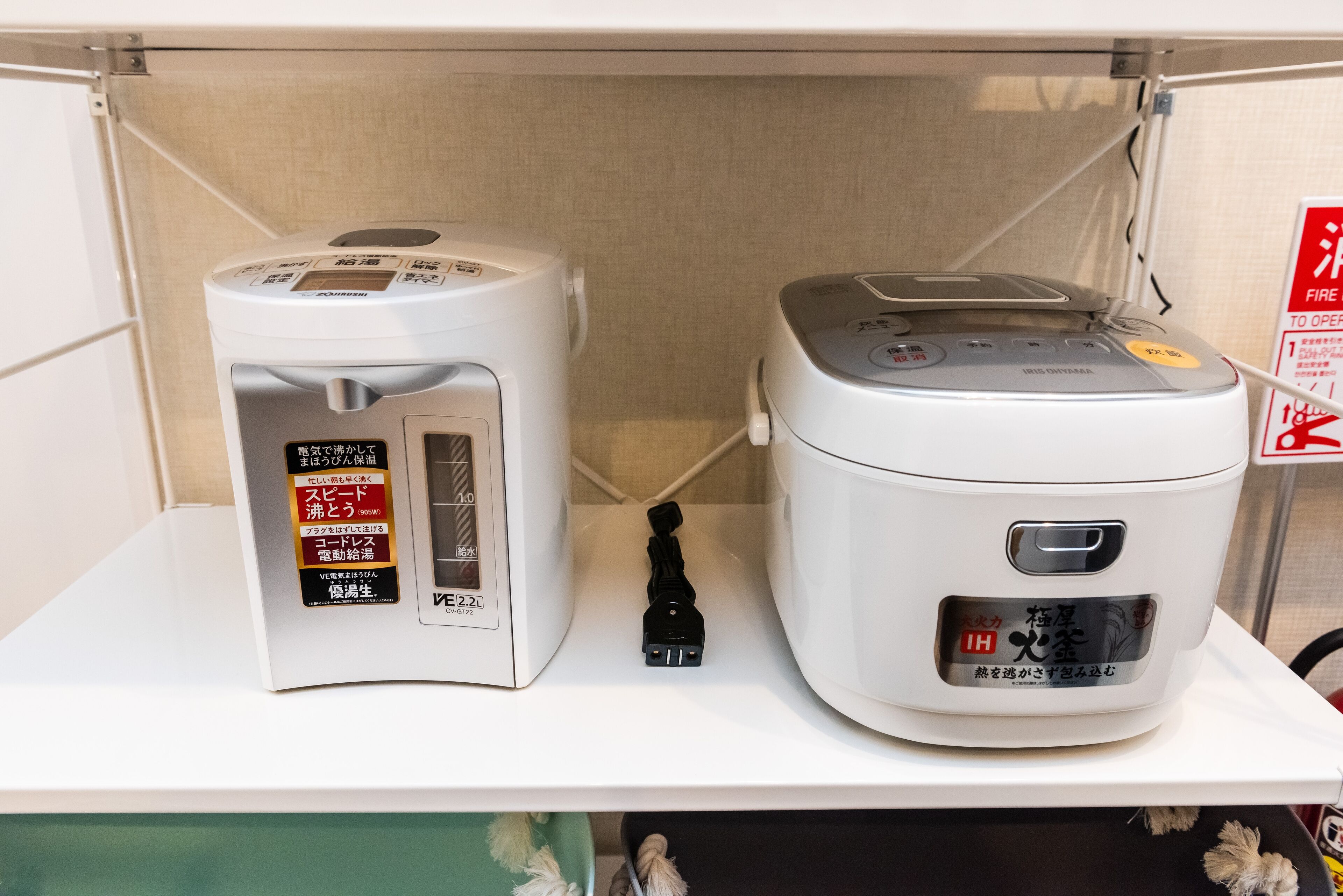 Two rice cookers on a shelf with a fire safety sign in the background.