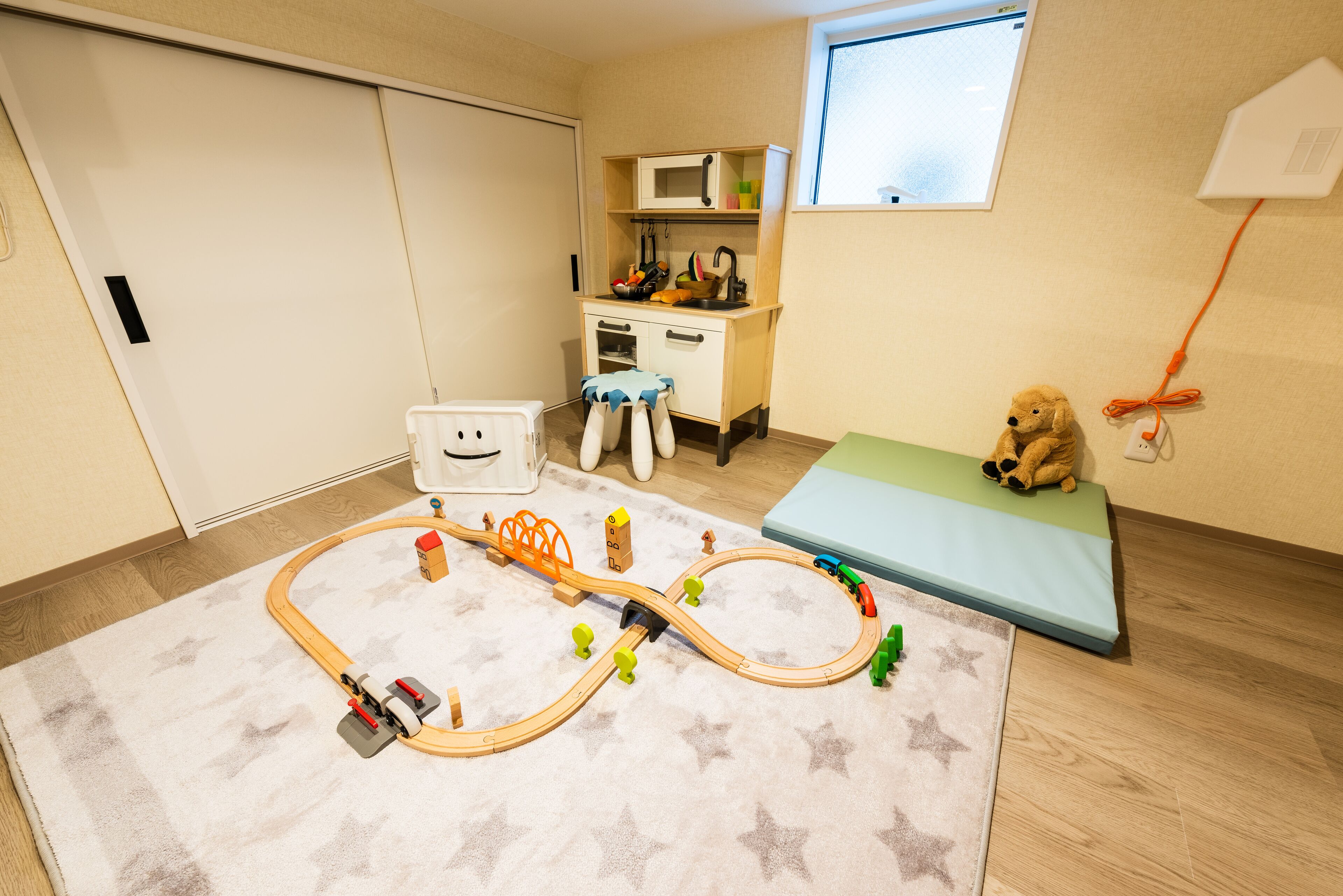 A child's playroom with a train set, a desk, a bed, and a teddy bear.