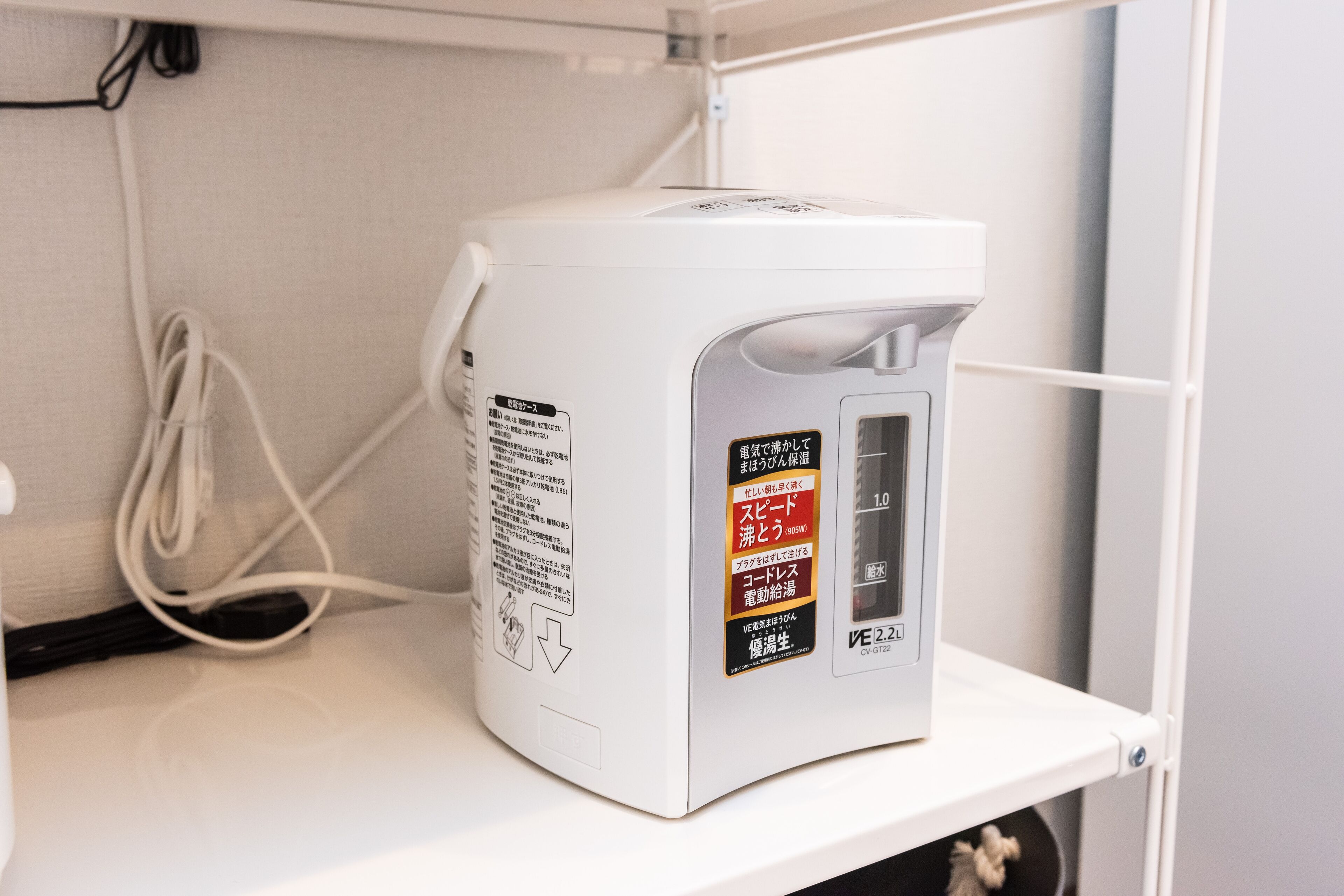 Uma máquina de café branca com instruções em japonês e um cabo de alimentação ligado.