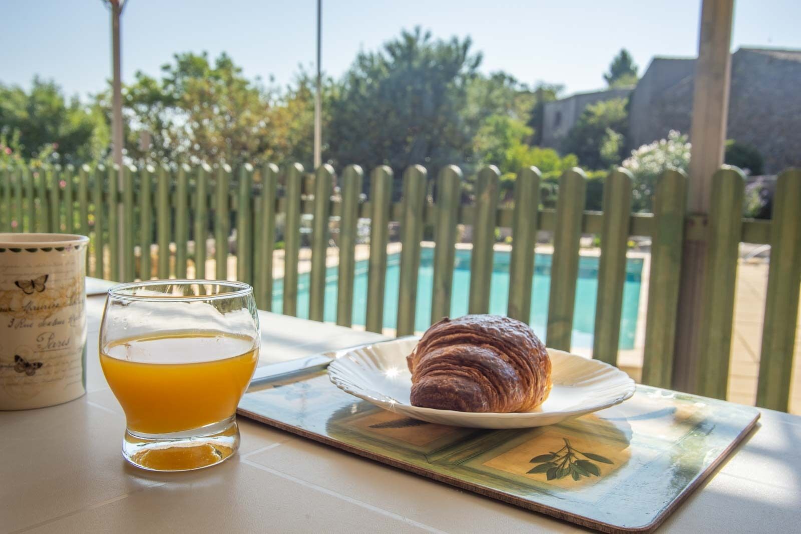 Ett bord med ett glas apelsinjuice, en tallrik med en croissant och en dekorativ mugg.