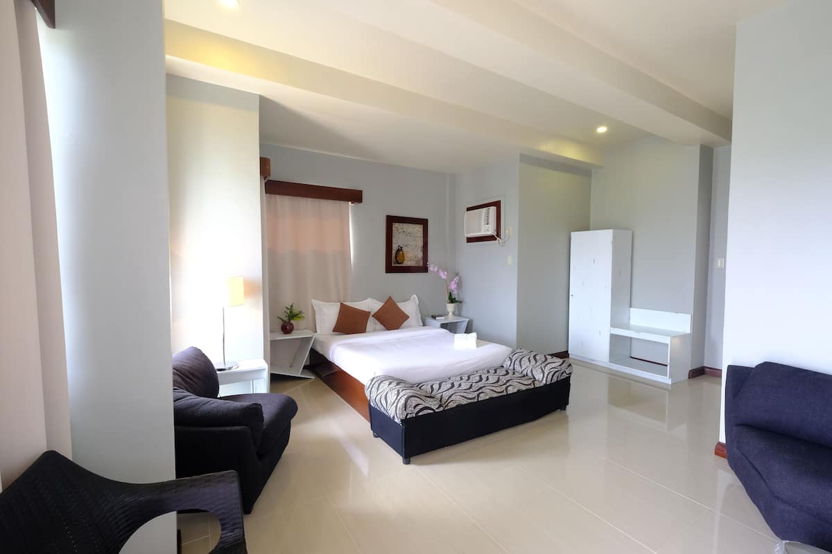 A modern hotel room with a large bed, a desk, a chair, a wardrobe, and a TV.