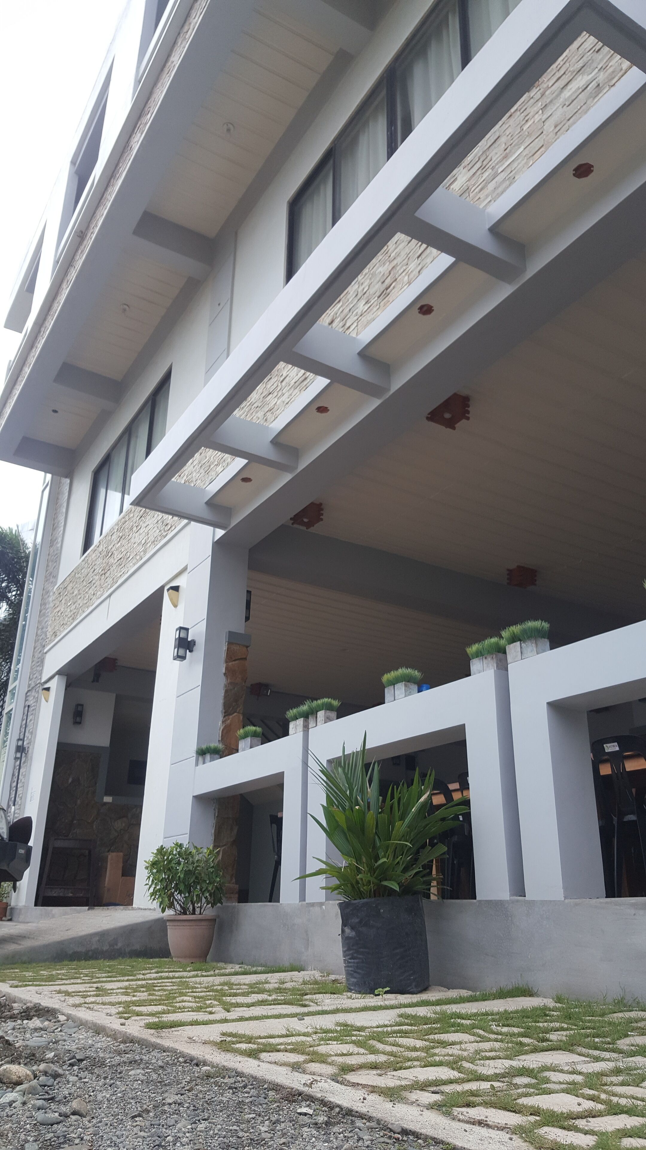 Un edificio moderno con techo plano, amplios ventanales y un área de entrada cubierta con plantas en macetas.