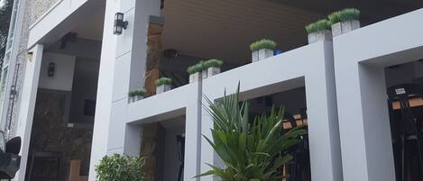 Un edificio moderno con techo plano, amplios ventanales y un área de entrada cubierta con plantas en macetas.