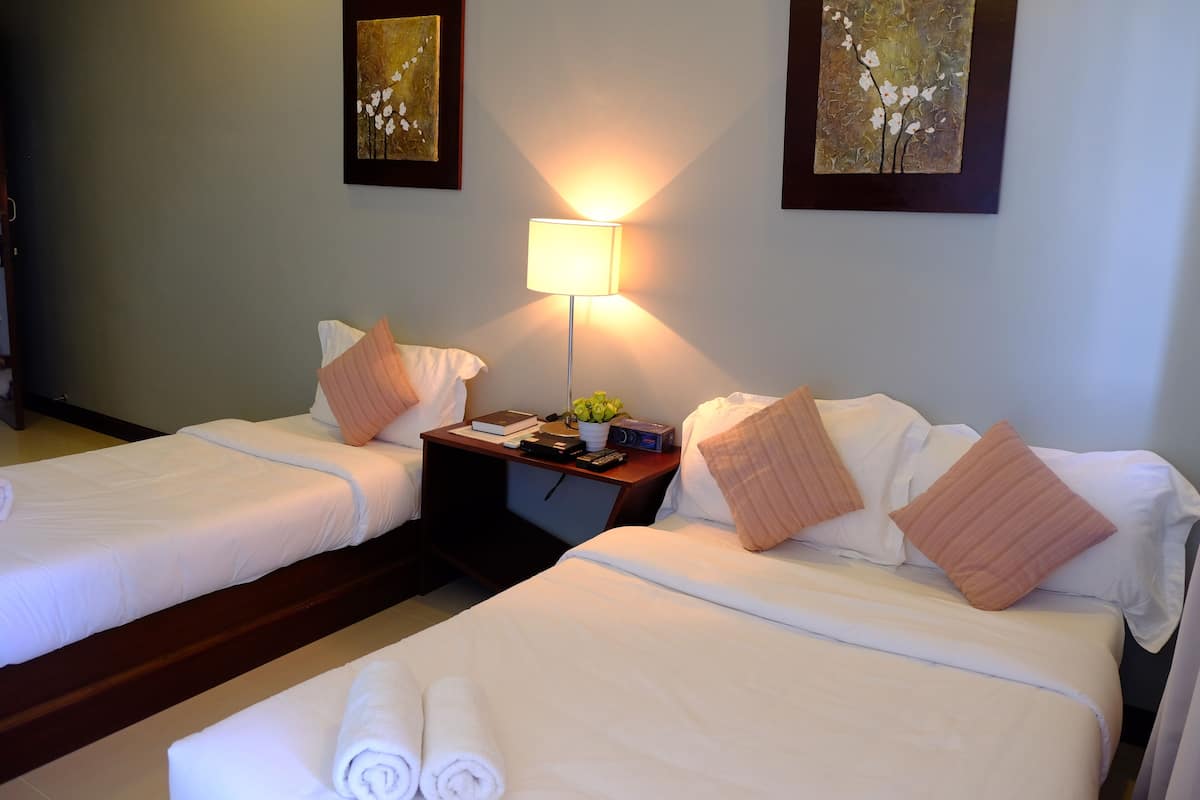 A hotel room with two beds, a nightstand with a lamp, and artwork on the walls.