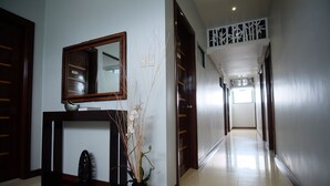 A hallway with a mirror, a vase with dried plants, and a door with a decorative panel. - Pacific Waves Inn Annex (Baler)
