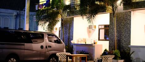 Una camioneta estacionada frente a un edificio con un patio, que incluye una mesa y sillas, y un pequeño jardín con plantas.