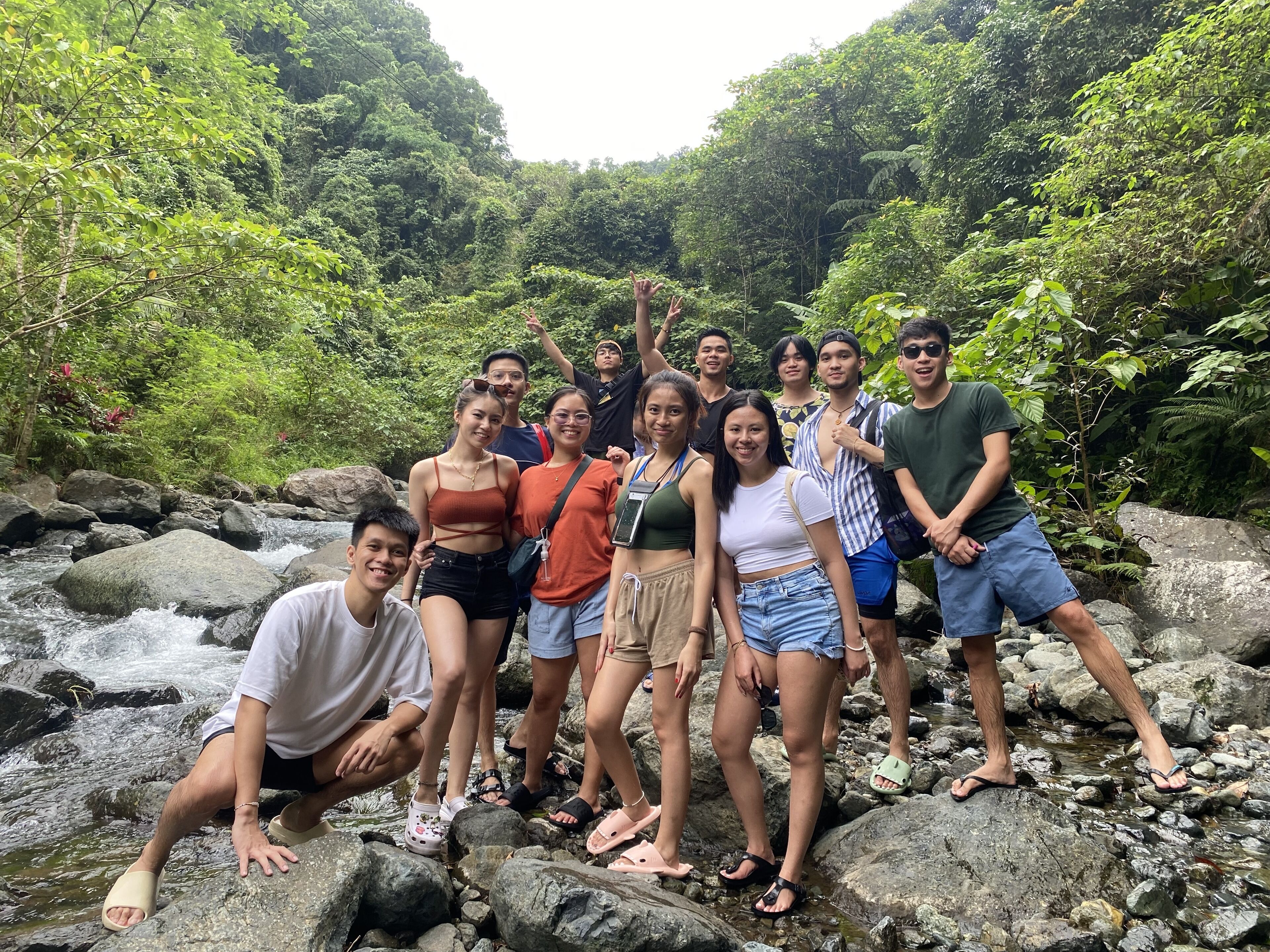 A group of people standing on rocks by a flowing stream in a lush, green forest.