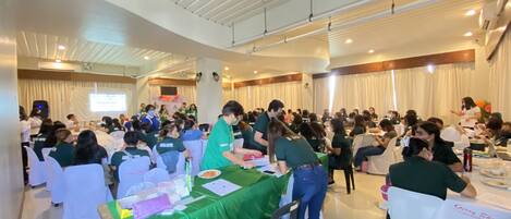 Una sala de conferencias con mesas redondas, sillas blancas y mantel verde.