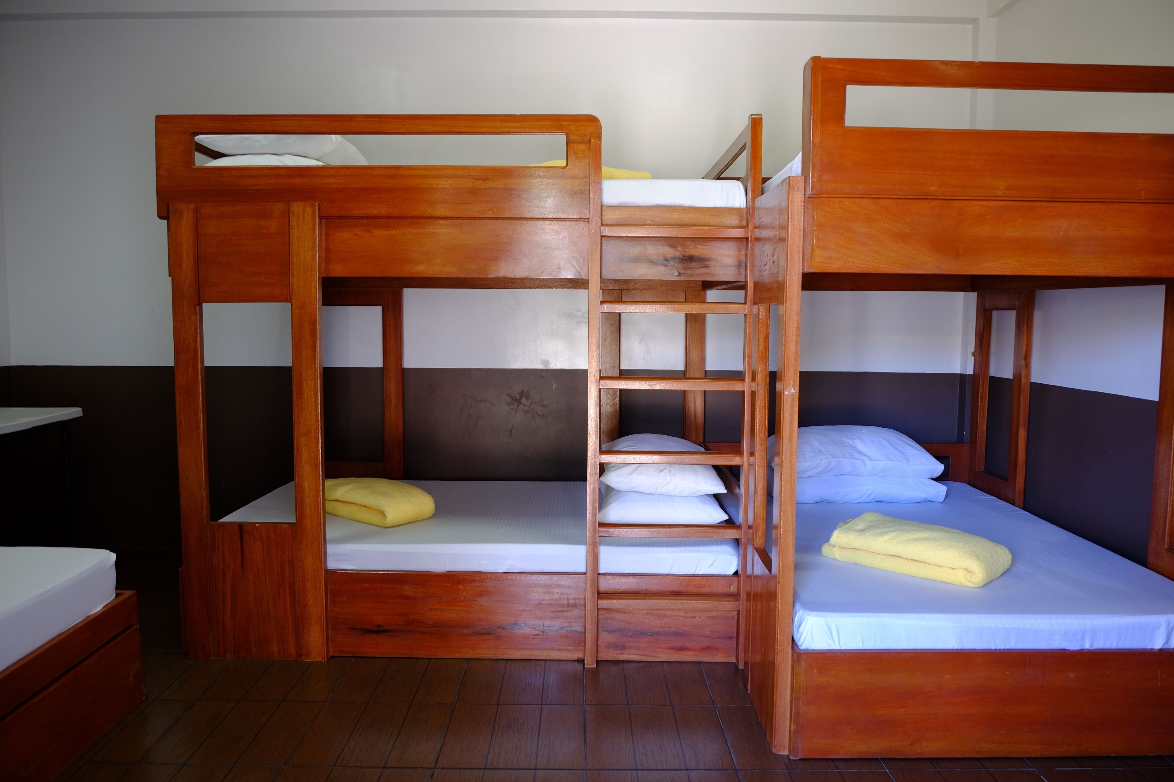 Ein Zimmer mit zwei Holzbettgestellen, jeweils ausgestattet mit Matratze und Kissen, verbunden durch eine Leiter.