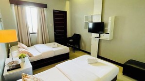 A hotel room with two beds, a TV mounted on the wall, a desk with a lamp, and a window with curtains. - Pacific Waves Inn Annex (Baler)
