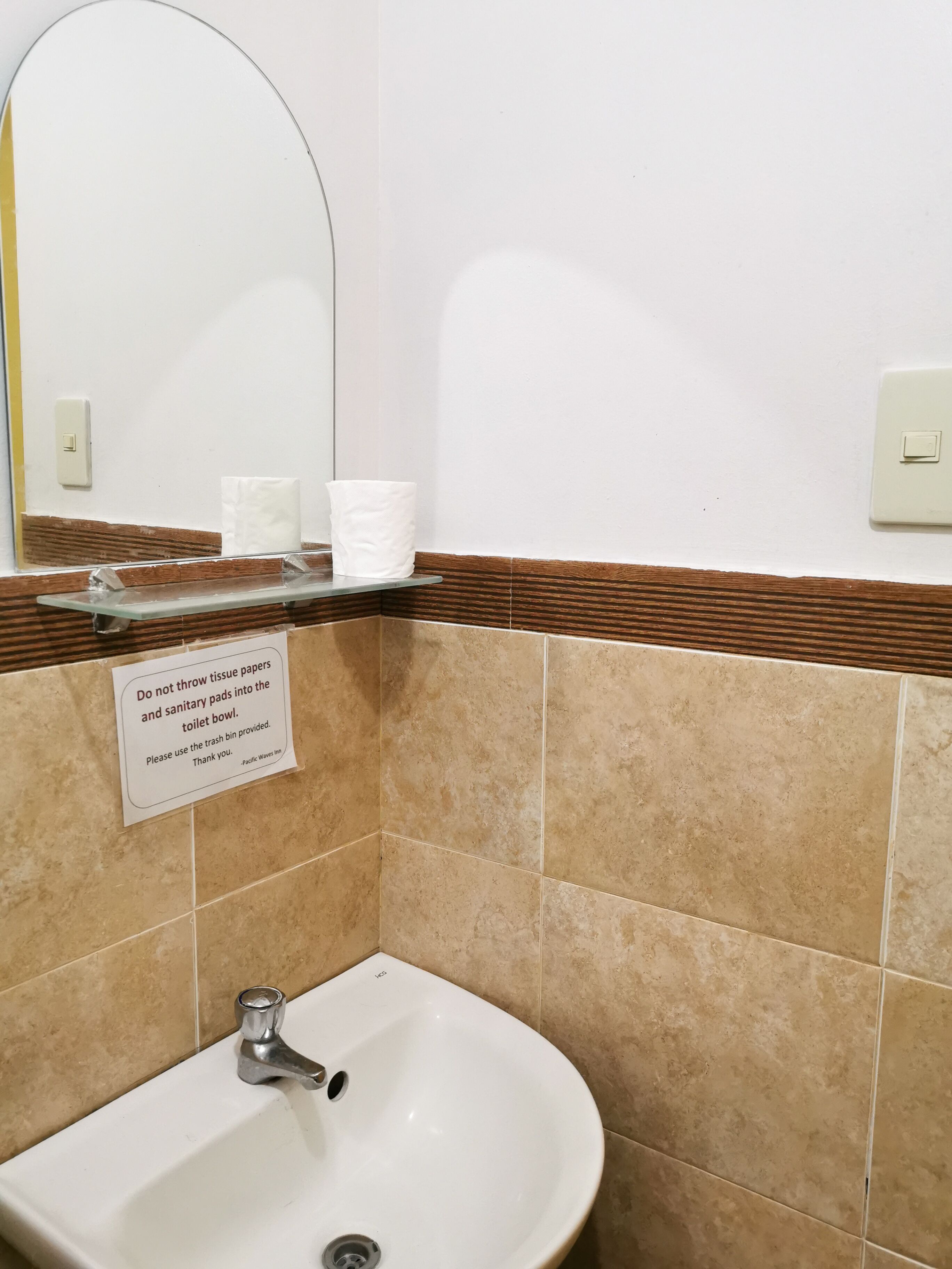 Ein Badezimmer mit Waschbecken, Spiegel und einem Schild, das darauf hinweist, Damenbinden und Toilettenpapier nicht in die Toilette zu werfen.
