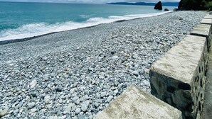 A pebbled beach with a stone wall and a rocky outcrop in the distance. - Pacific Waves Inn Annex (Baler)