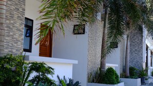 A modern building with a stone facade, large windows, and a well-maintained garden with various plants and a pathway. - Pacific Waves Inn Annex (Baler)