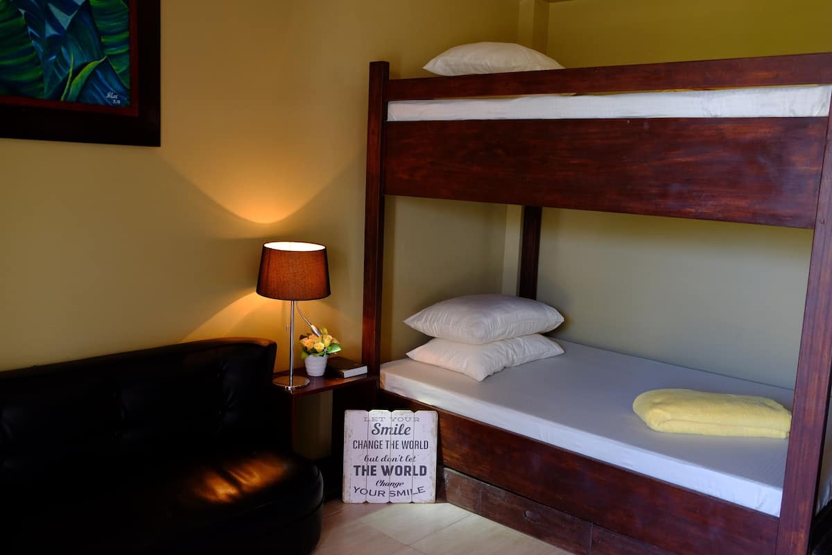 A bunk bed with white bedding, a bedside lamp, a small table with a flower, and a motivational sign.