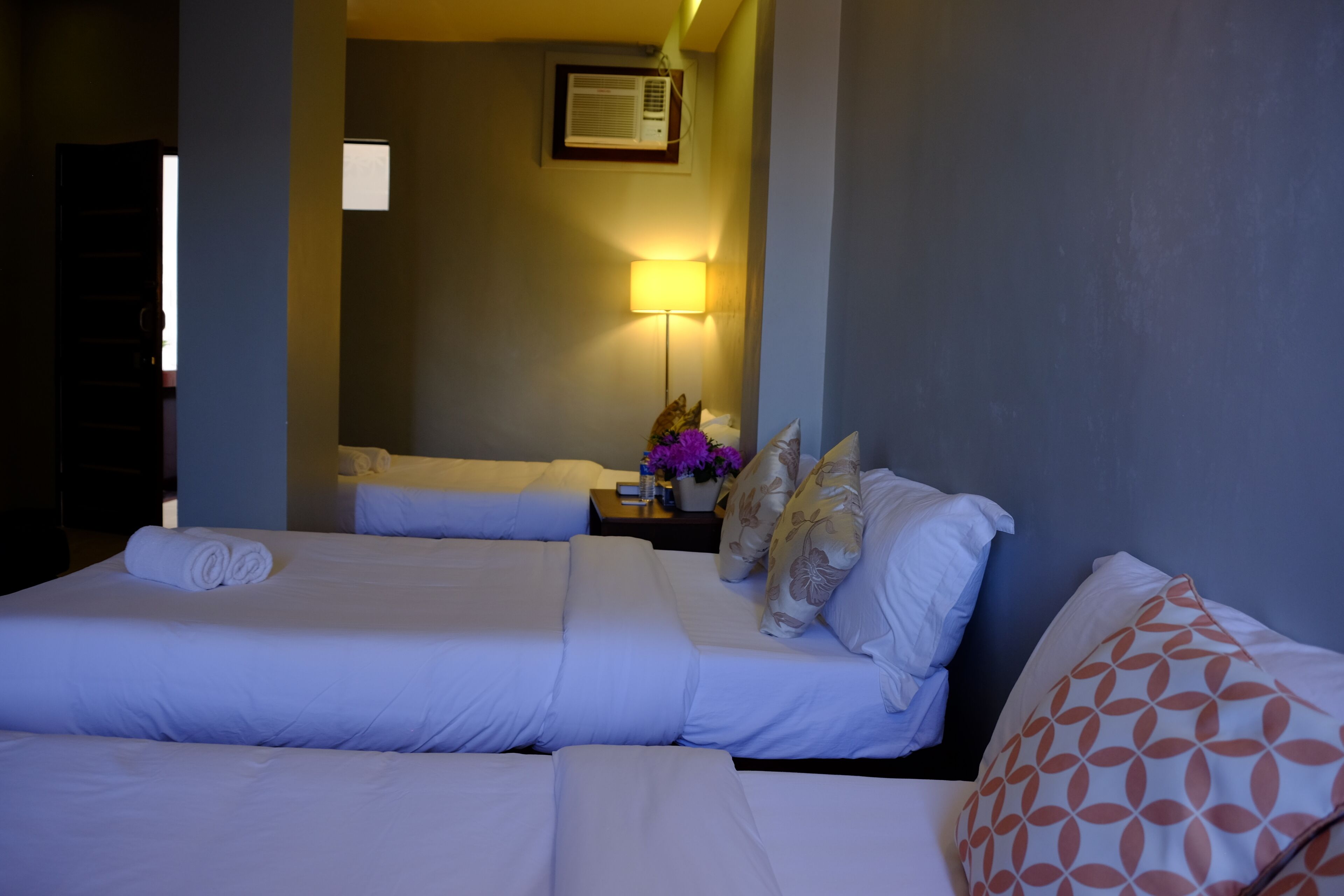 Quarto de hotel com duas camas, mesa de cabeceira com abajur e ar condicionado fixado na parede.