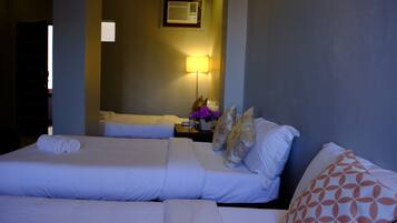 Quarto de hotel com duas camas, mesa de cabeceira com abajur e ar condicionado fixado na parede.