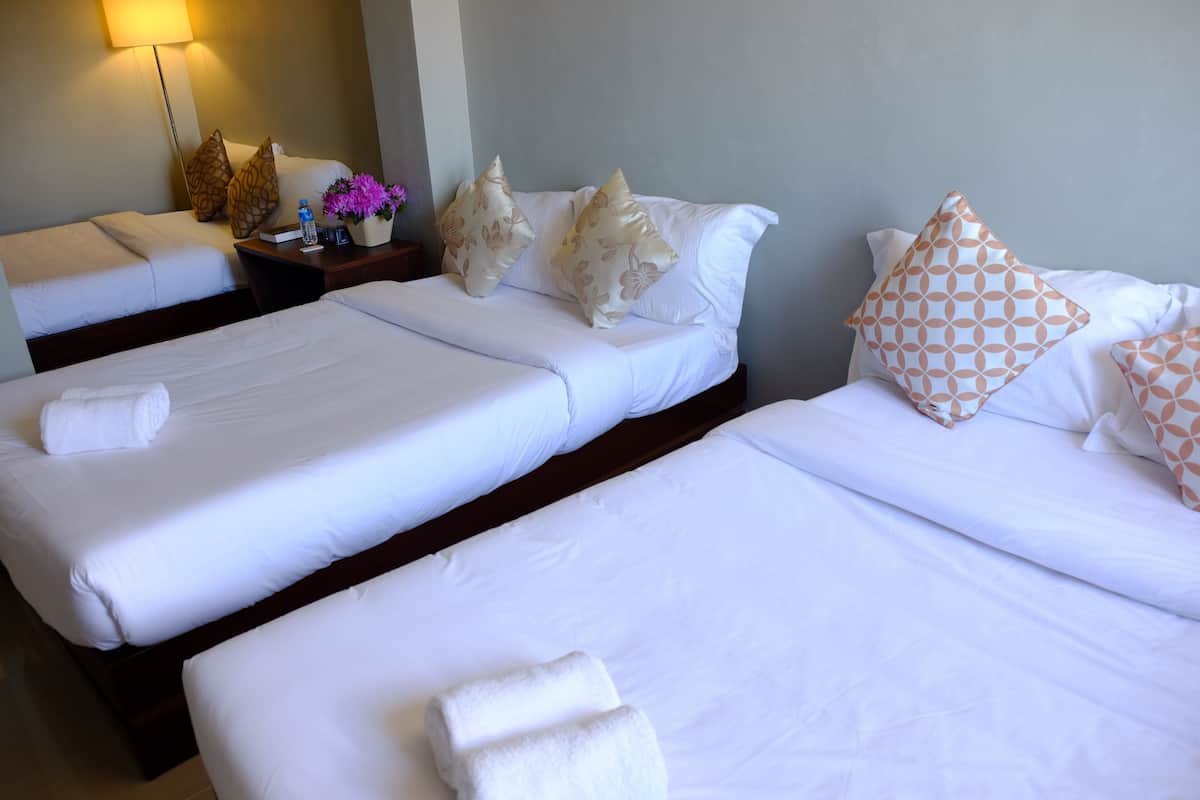 A hotel room with two single beds, a nightstand with a lamp, a vase with flowers, and a water bottle.