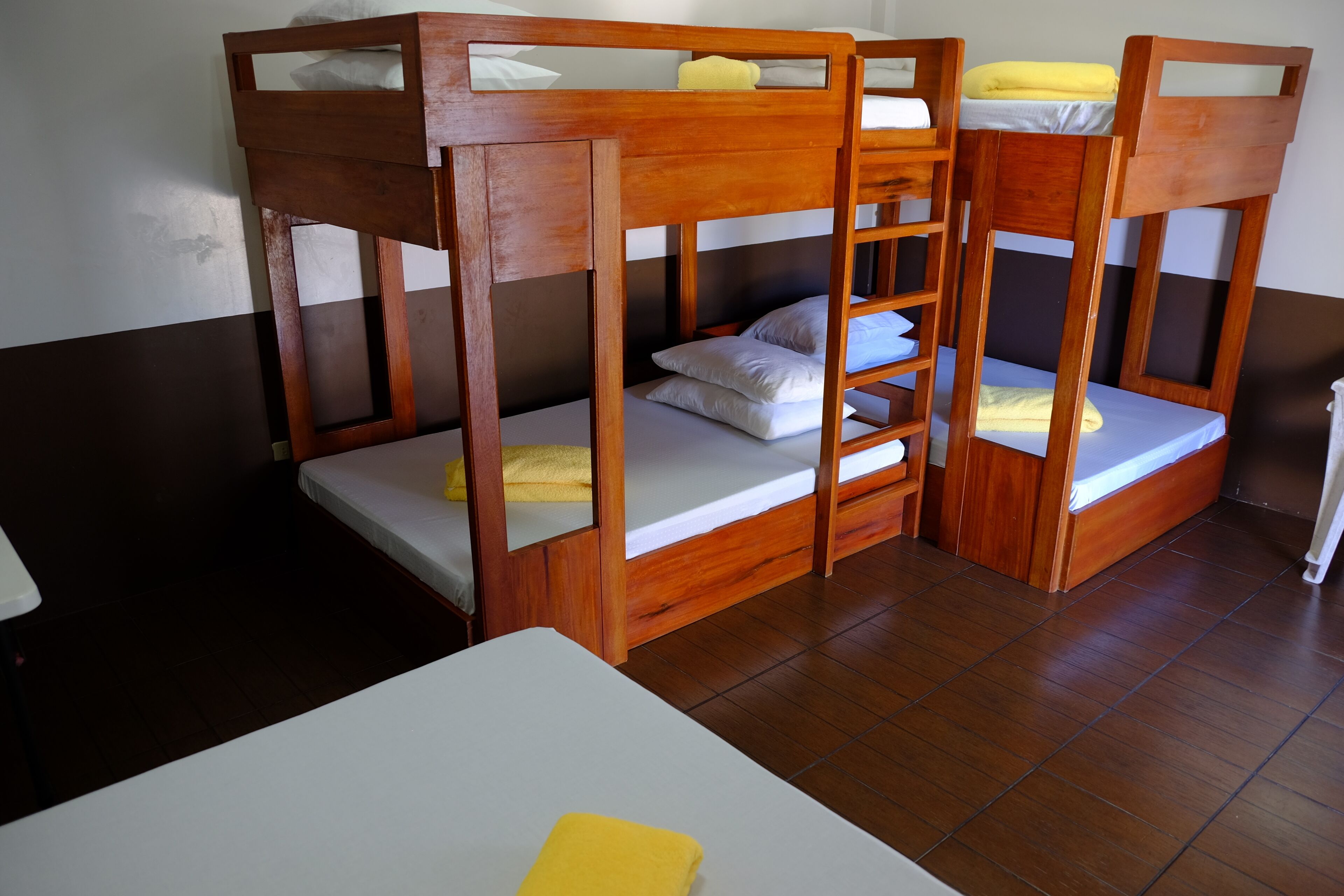 A bunk bed room with wooden frames, white bedding, and a white table.