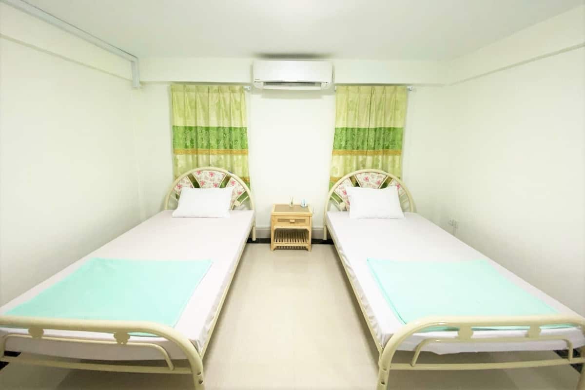 A room with two single beds, a small bedside table with a lamp, and an air conditioning unit on the wall.