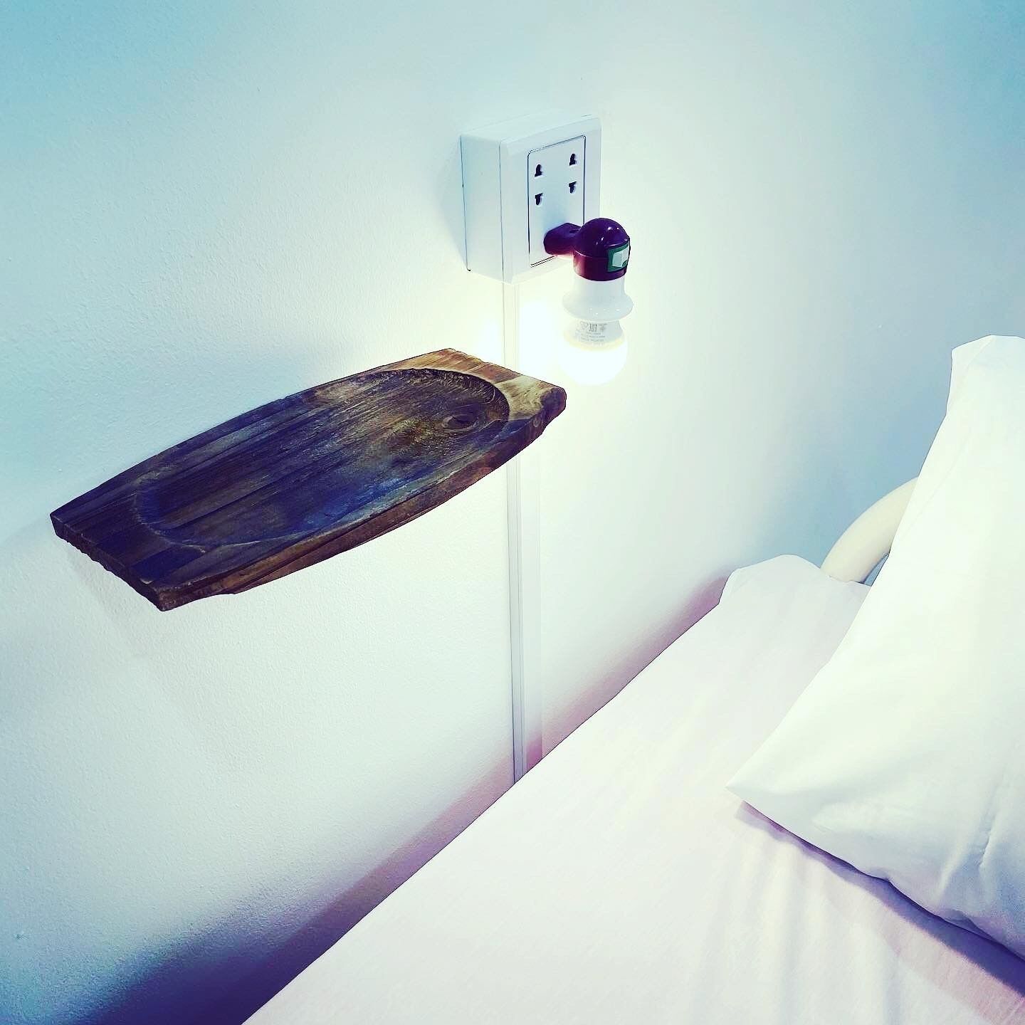 Ein Nachttisch mit einer Holztablett und einer an der Wand befestigten Lampe.