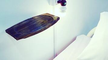 Una mesita de noche con una bandeja de madera y una lámpara de pared.