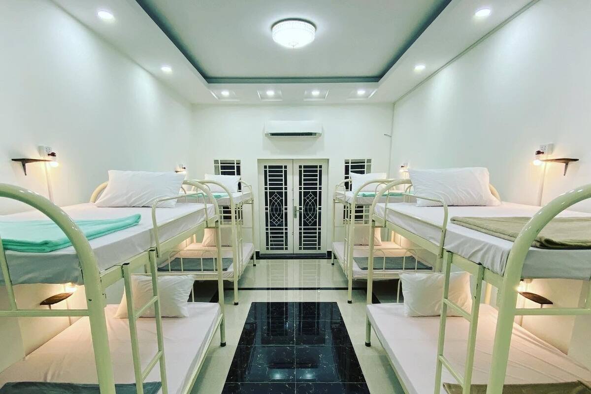 A room with bunk beds arranged in two rows, a central black marble pathway, and a door with a decorative grille.