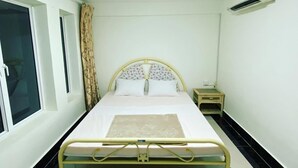 Habitación individual con una cama con cabecera, una mesita de noche, una ventana con cortinas y un equipo de aire acondicionado en la pared.