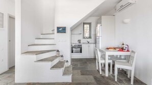 A modern kitchen with white cabinetry, a dining table with chairs, and a staircase leading to another level. - Villa Bianca Tzia (Kea)