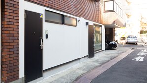 A building with a brick facade, a white door, and a parking area with a car. - Cross Bridge Ikebukuro (Tokyo)
