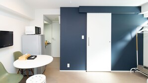 A modern hotel room with a white round table, a green chair, a flat-screen TV, a microwave, and a wardrobe with a sliding door. - Cross Bridge Ikebukuro (Tokyo)