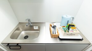 A modern kitchen with a stainless steel sink, a kettle, and a wooden box containing tea and snacks. - Cross Bridge Ikebukuro (Tokyo)