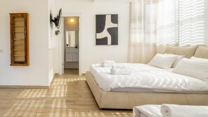 Un dormitorio con una cama grande, una escalera de madera, un baño visible a través de una puerta abierta y un cuadro abstracto moderno en la pared.