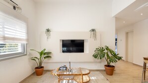 Una sala de estar moderna con un televisor de pantalla plana, dos plantas en macetas, una mesa redonda de centro y un sofá.