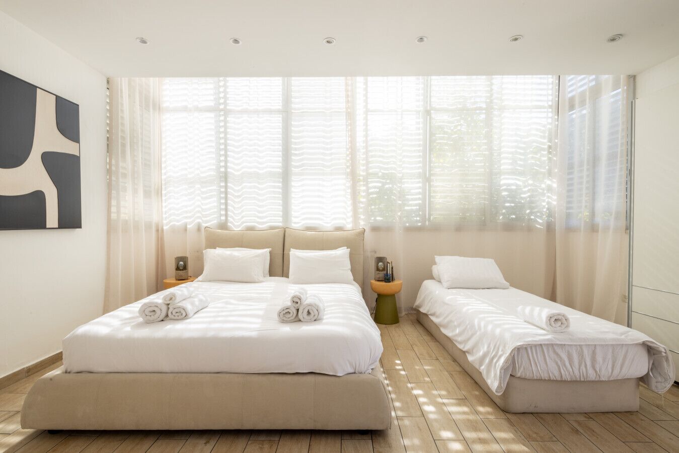 Una camera da letto moderna con due letti, un'ampia finestra con tende leggere e un arredamento minimalista.