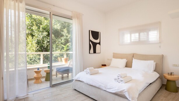 Habitación de hotel moderna con una cama grande, un balcón con plantas en macetas y vistas al exterior.