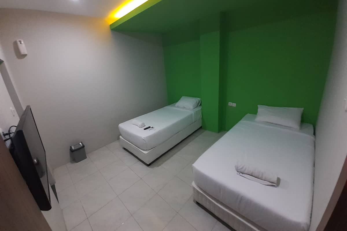 Een kleine, moderne kamer met twee bedden, een televisie en een prullenbak.