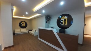 A hotel reception area with a wooden floor, white sofas, and a reception desk. - TriDD 01 Sriwijaya Hotel (Mataram)