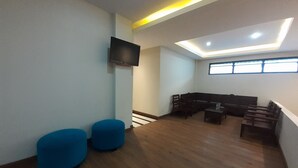 A modern waiting area with a flat-screen TV mounted on the wall, blue cushioned seating, and a wooden bench. - TriDD 01 Sriwijaya Hotel (Mataram)